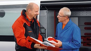 Ein Vissmann Mitarbeiter zeigt einem Kunden, einen Ordner vor einem Firmenbulli