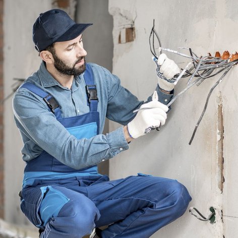 Ein Elektroniker der auf einem Rohbau die Kabel aus der Wand zieht