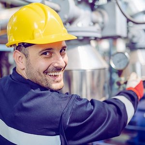 Ein Anlagenmechaniker mit einem Bauhelm, vor einer Heizungsanlage